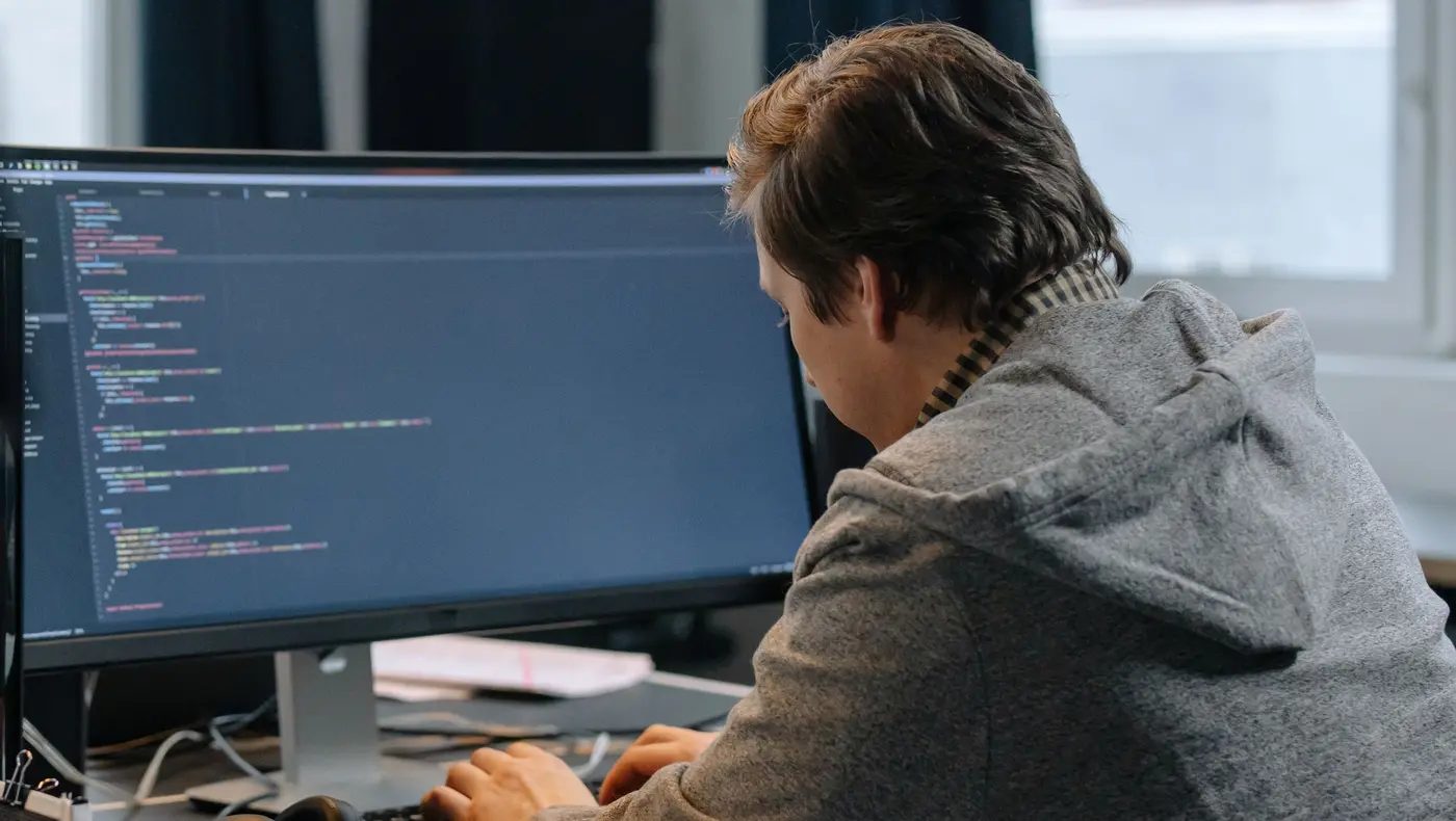 A developer in a grey hoodie writing code on a large monitor