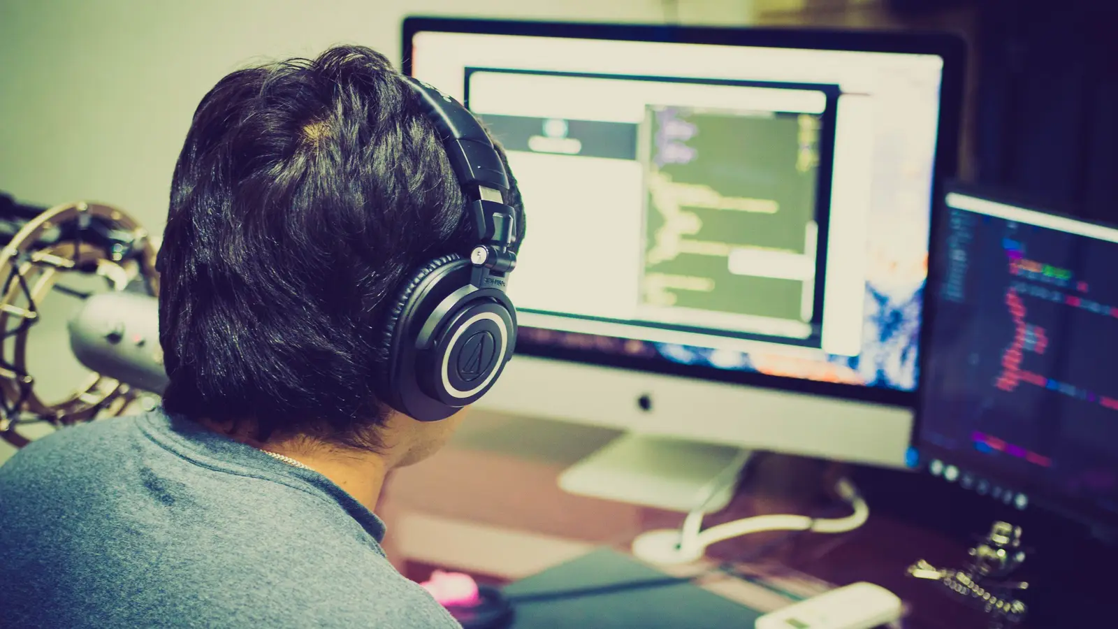 A developer in headphones working at two monitors, seen from behind