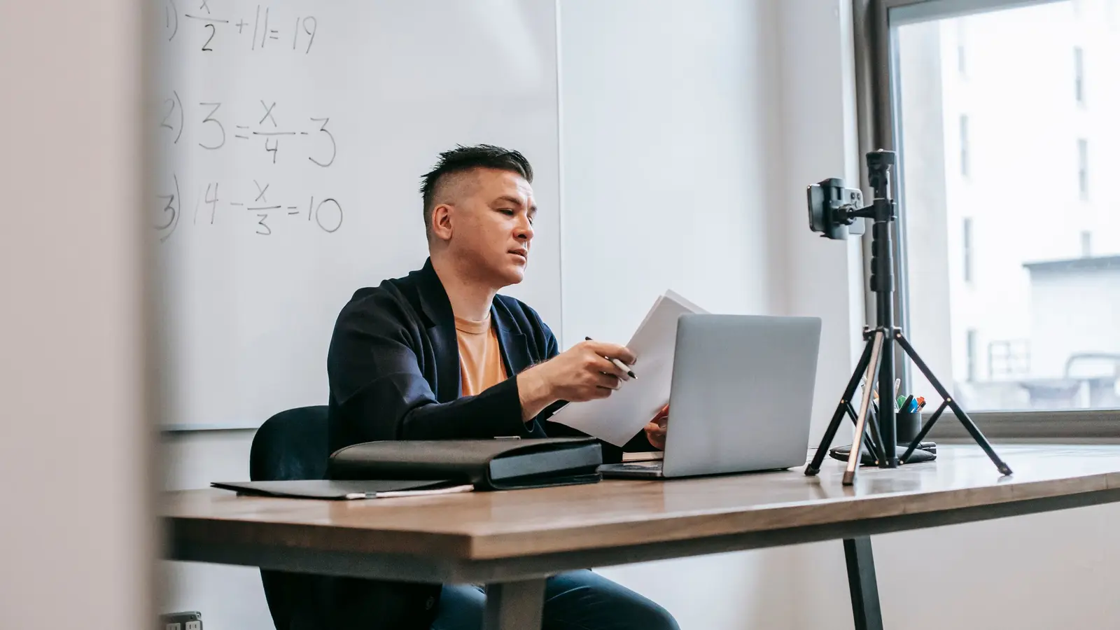 A teacher recording an online maths lesson with a laptop and a phone on a tripod