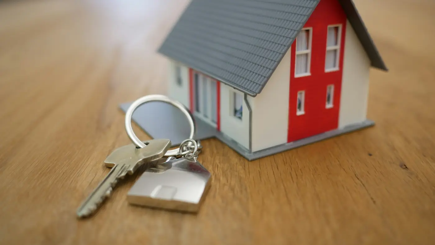 A small model house beside a set of keys on a wooden surface.