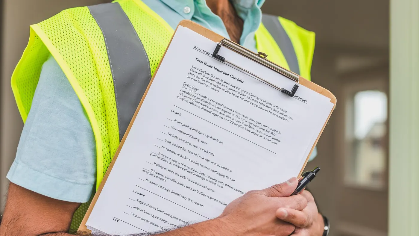 An inspector in a high-visibility vest holding a checklist on a clipboard.