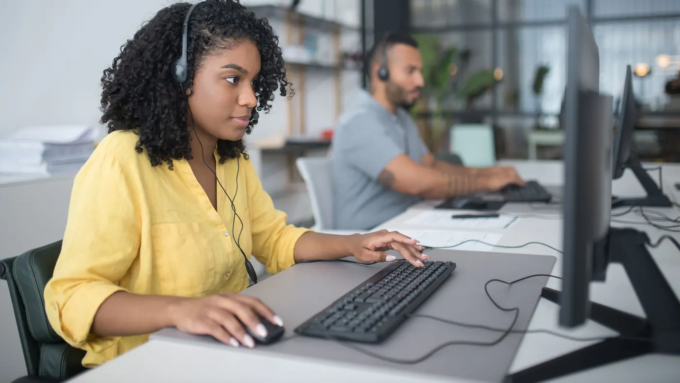 Two support agents wearing headsets at their desks in an office.