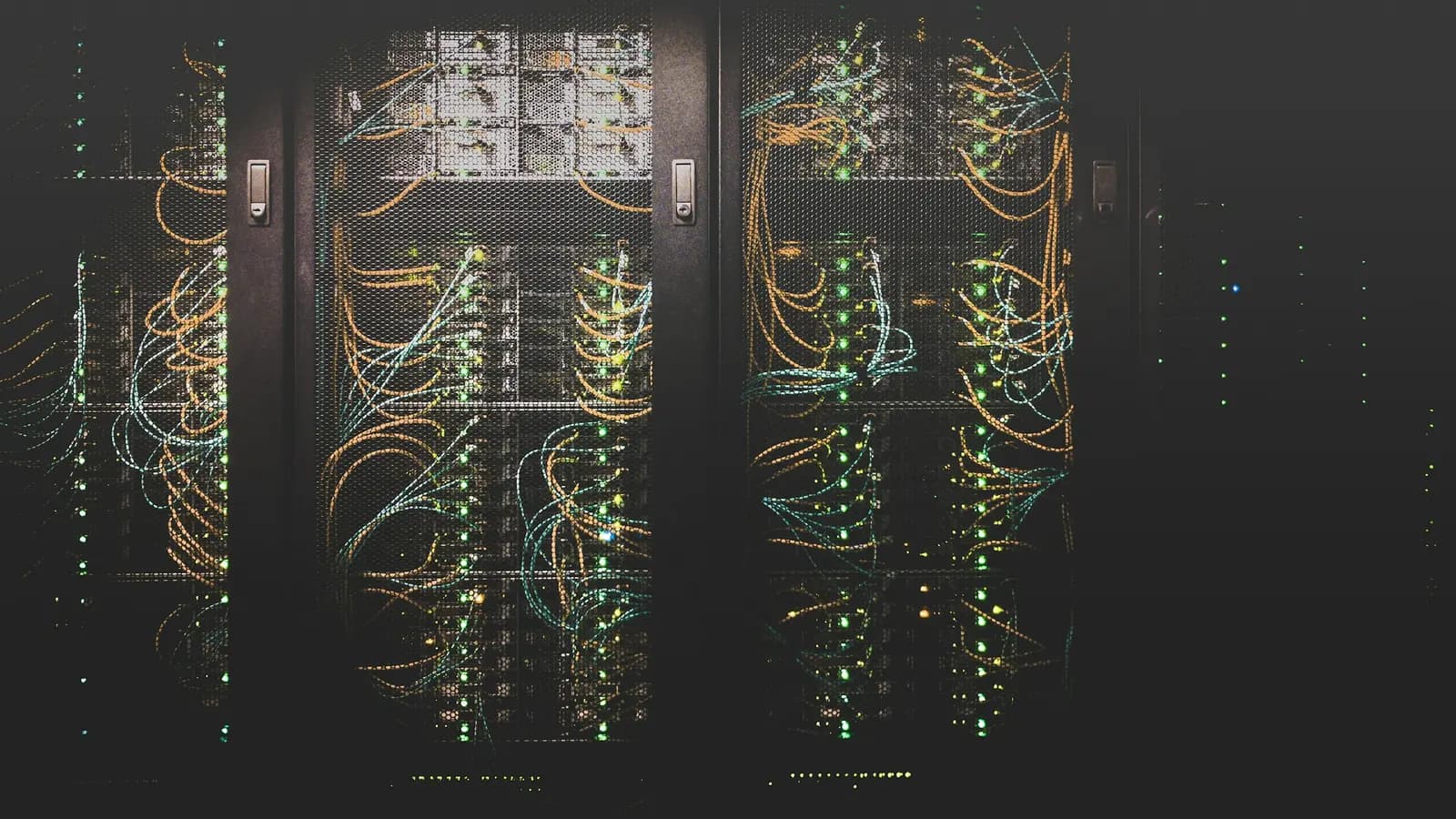 Racks of servers in a dark data centre, threaded with amber and cyan fibre optic cables and rows of green status lights.