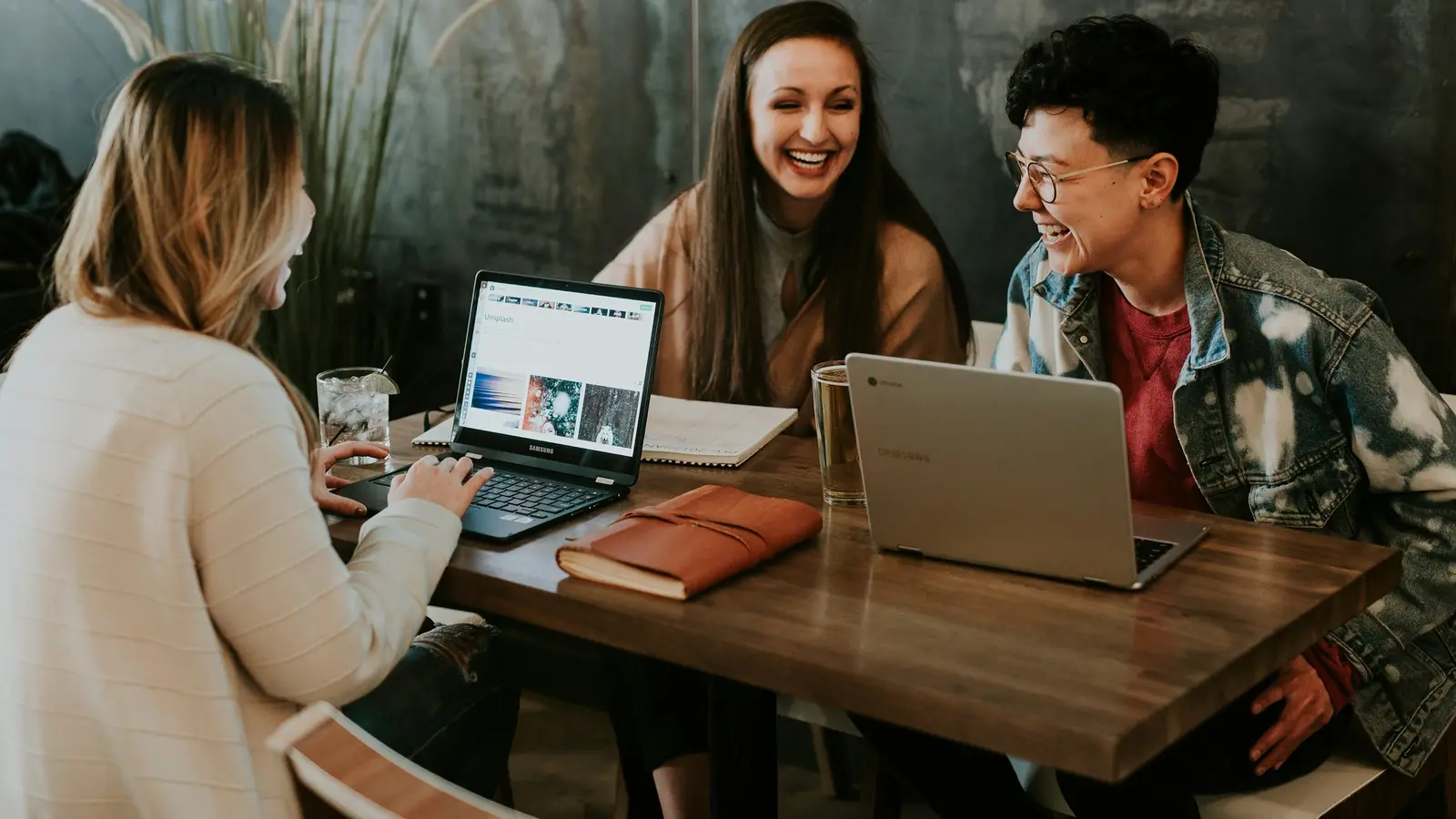 Three people in discussion around a laptop at a wooden table.