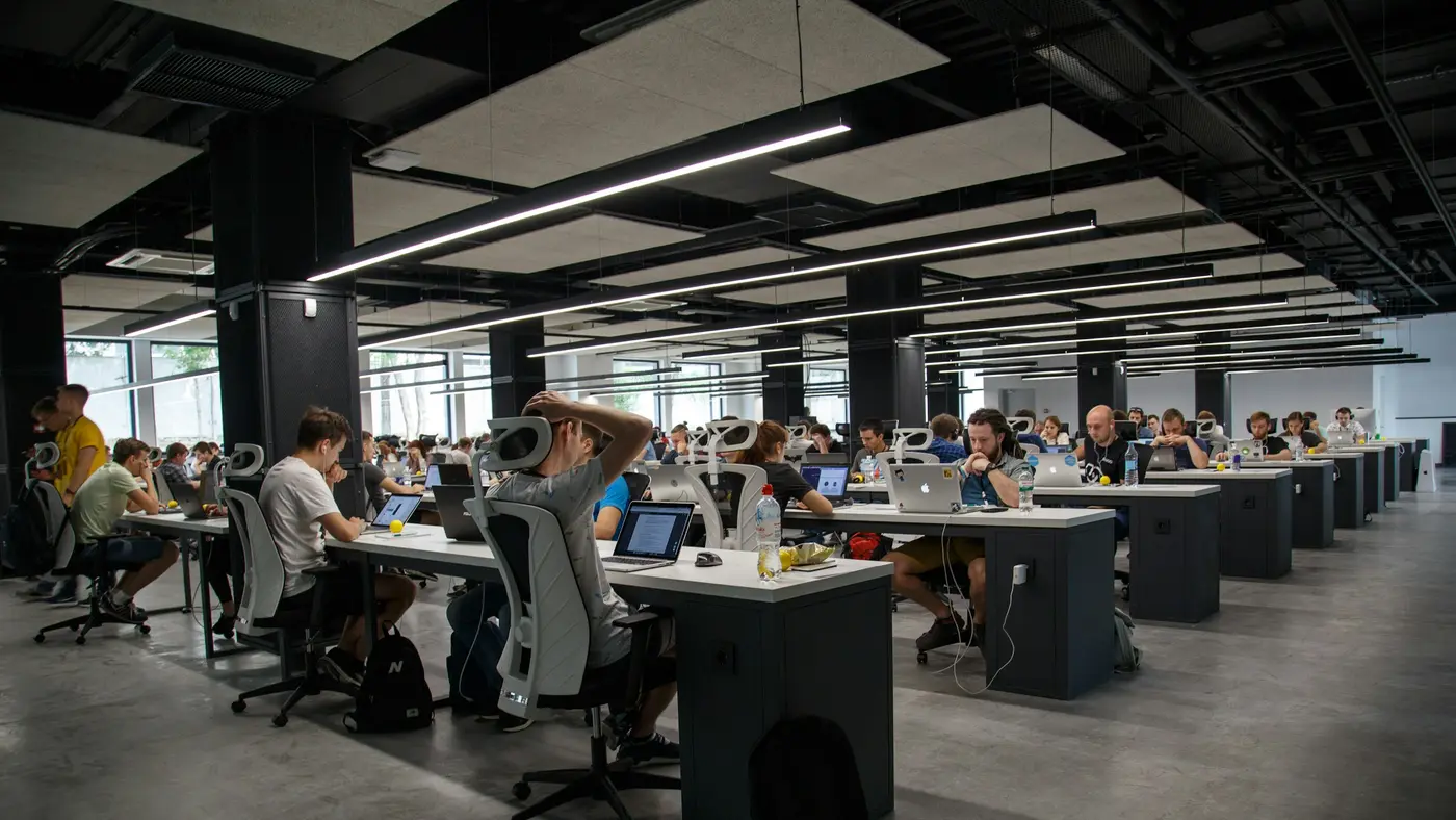 A large open-plan office seen from above, with many people working at long desks.
