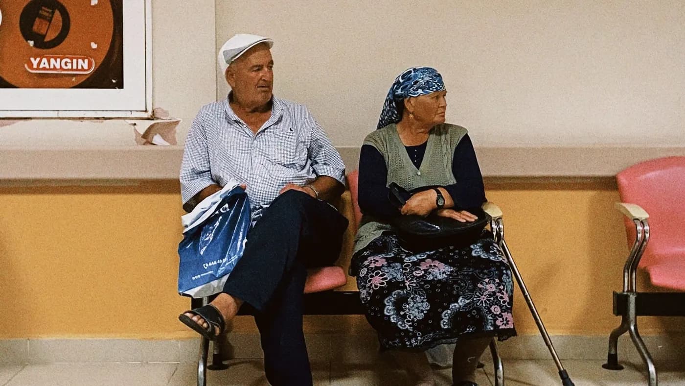 Two elderly patients sitting side by side on a bench in a clinic waiting area.