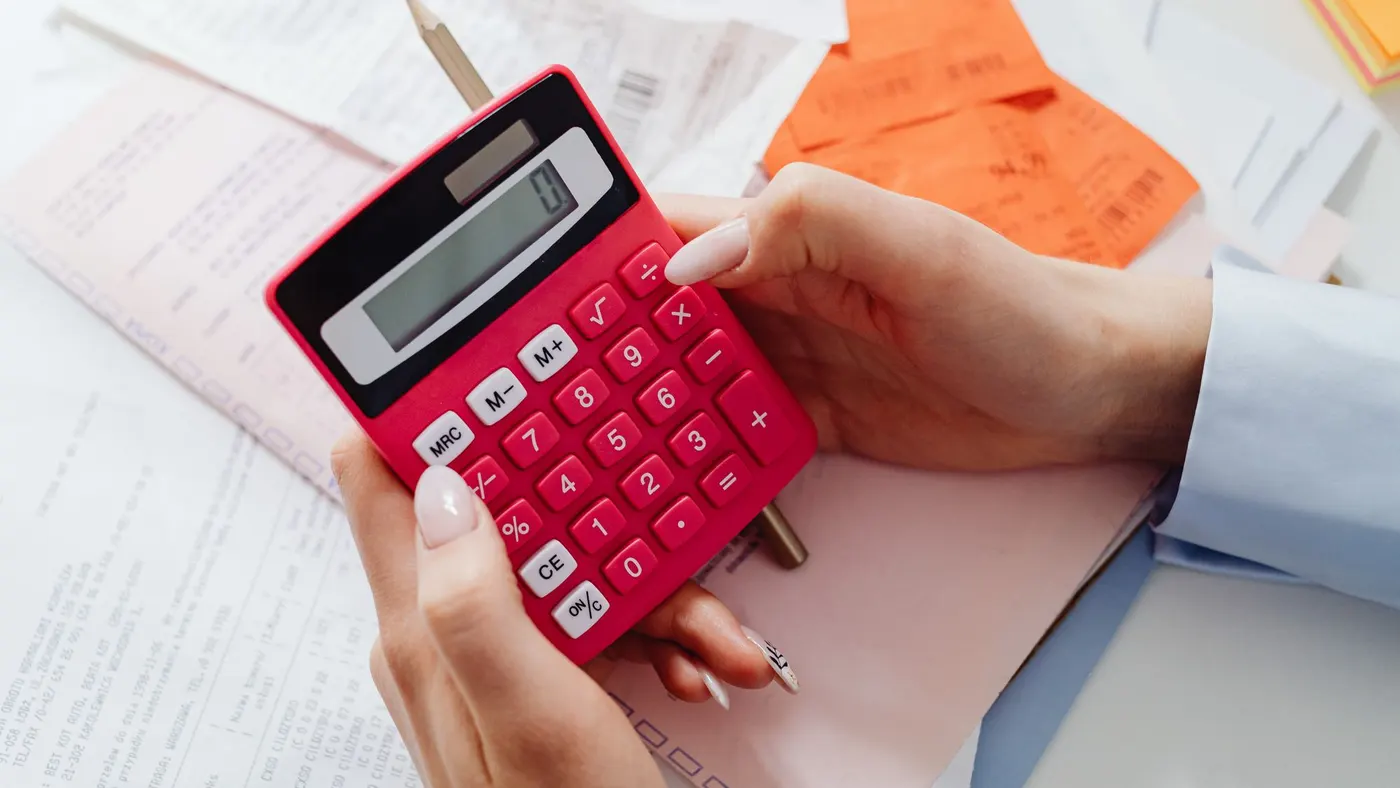 A person holding a red calculator over printed invoices and receipts.