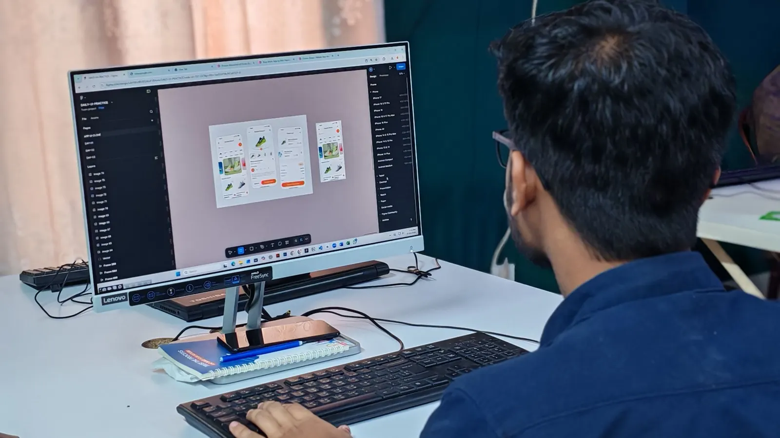 A designer at a desk working on app screens in a design tool on a large monitor.