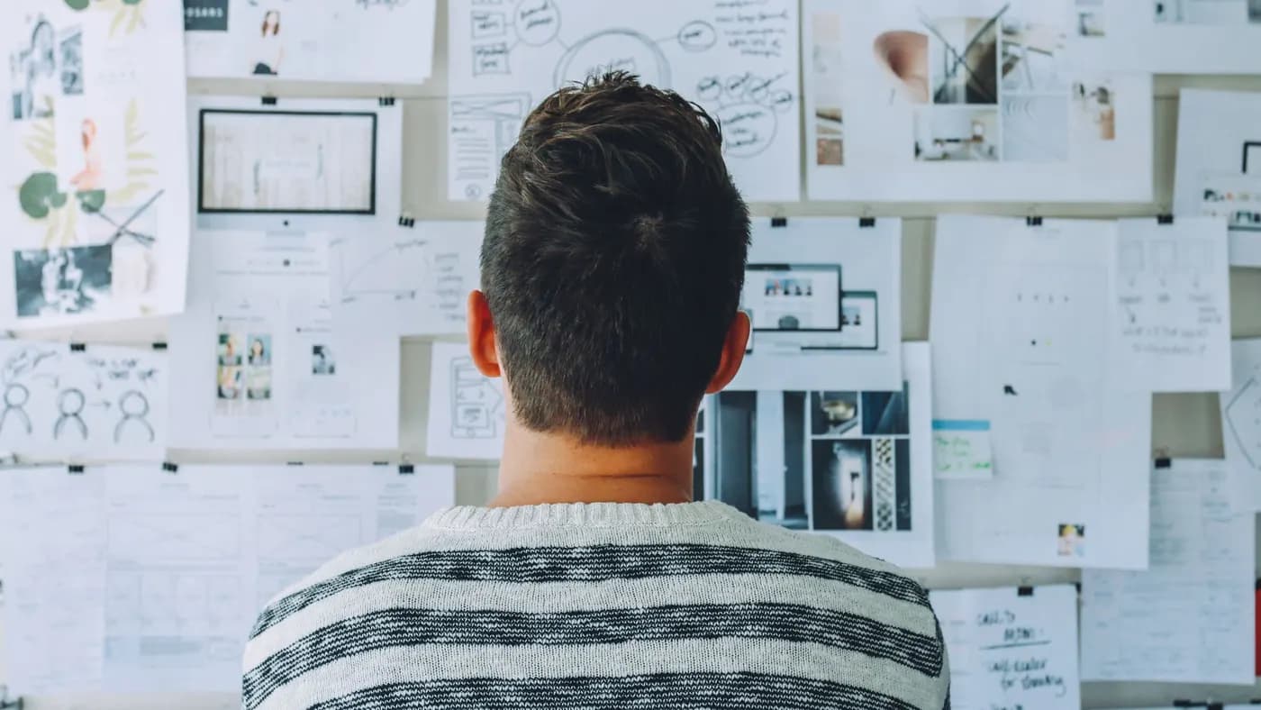 A person standing in front of a wall covered in pinned sketches and printed screen layouts.