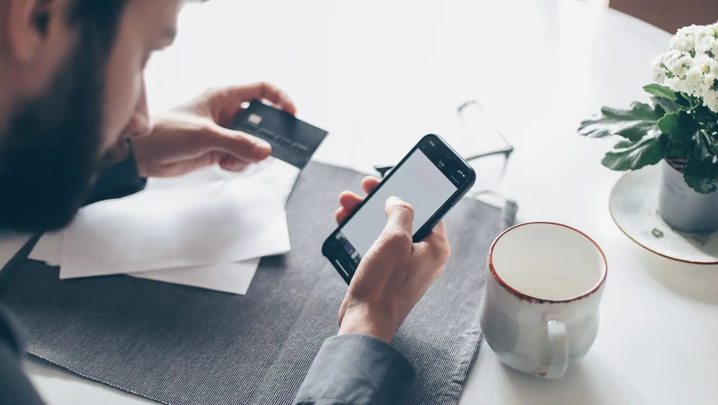 A person at a table paying on a smartphone while holding a bank card