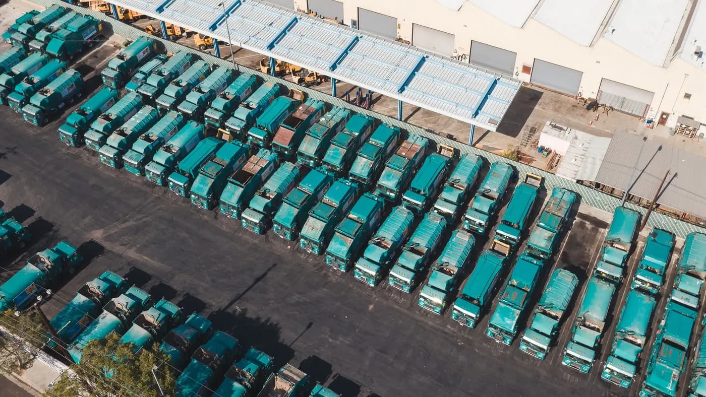 An aerial view of dozens of teal municipal trucks parked in rows at a depot.