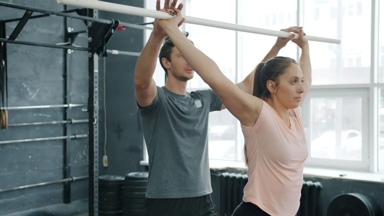 A trainer guiding a woman lifting a bar overhead in a gym