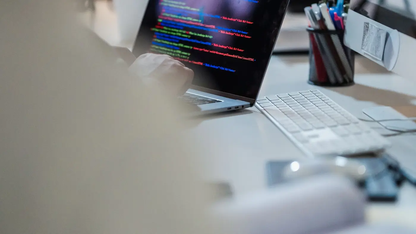 A laptop on a desk showing lines of code, with pens in a cup beside it.