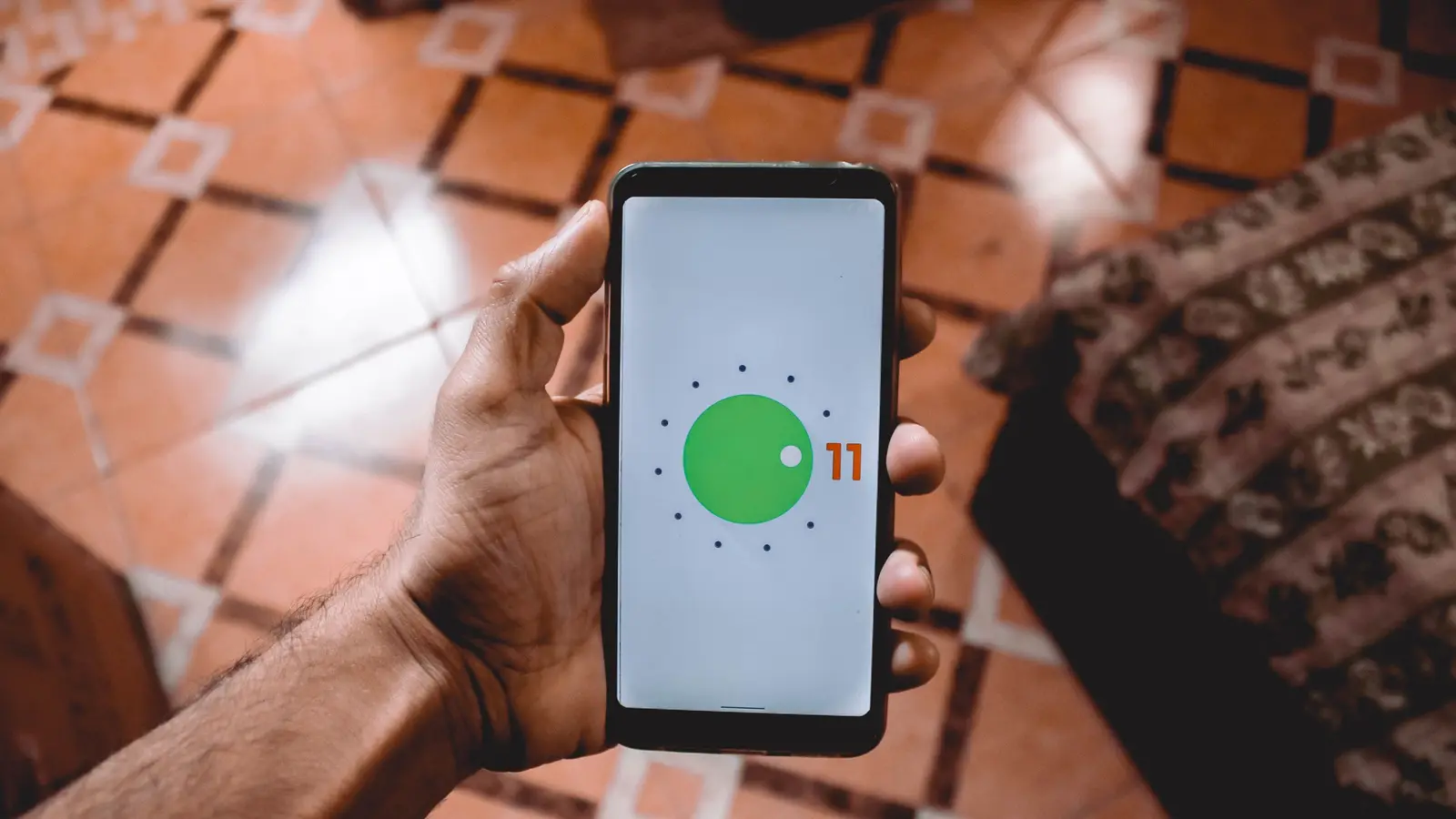 A hand holding up a phone showing the Android 11 logo on its screen.