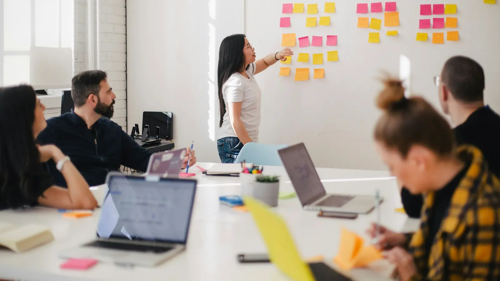A team in a meeting room, one person standing at a wall covered in sticky notes.