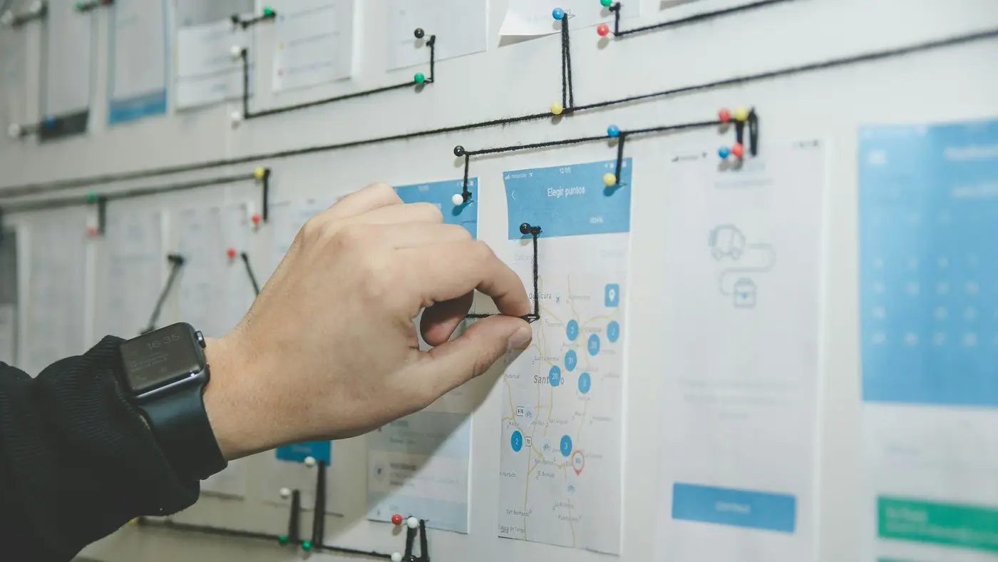 A hand pinning app wireframe sketches to a board.