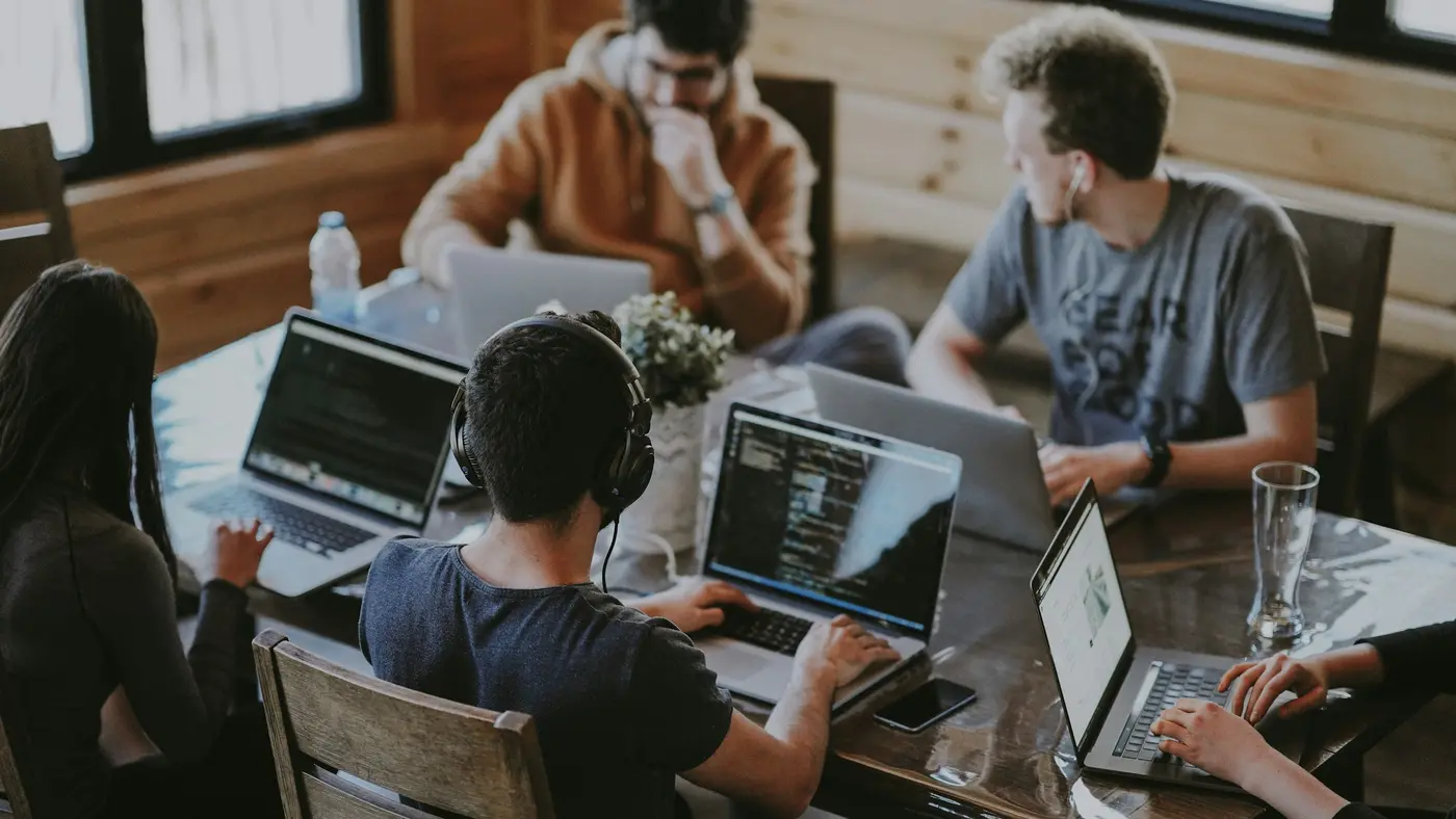 A group of people working together on laptops around a wooden table.