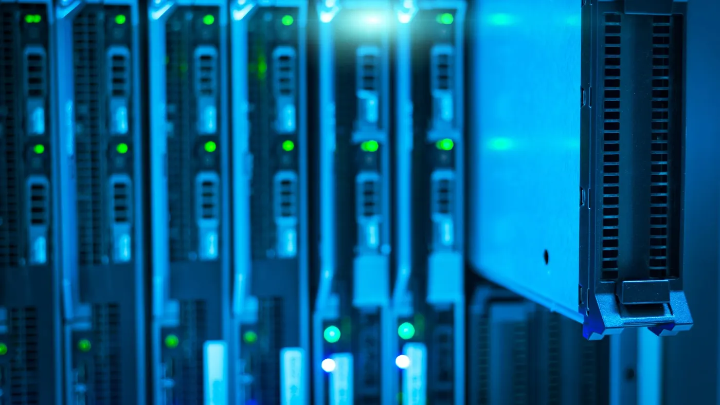 A row of blade servers in a rack with one tray pulled out, lit blue.
